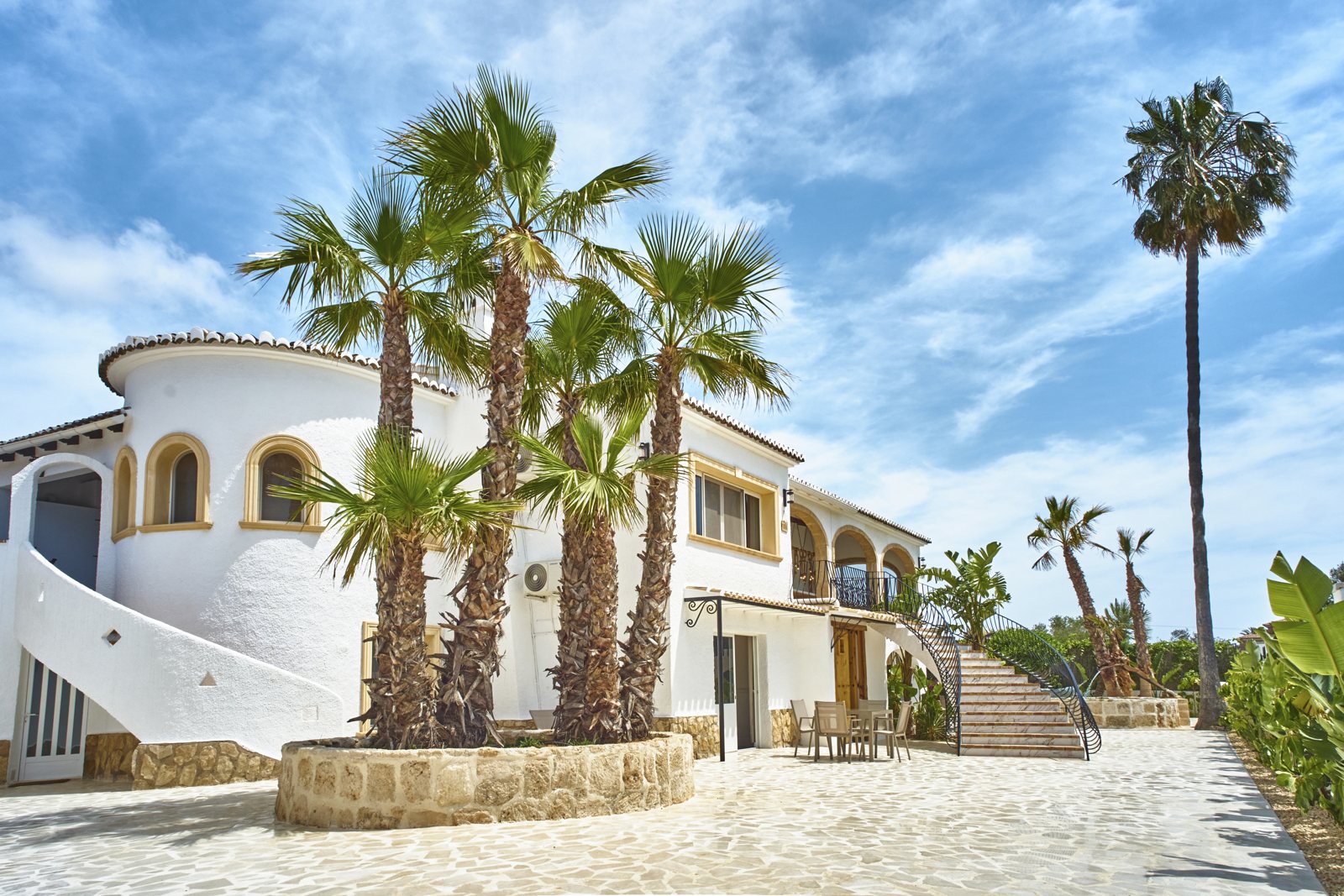 Fachada blanca de la villa con palmeras altas sobre cielo azul