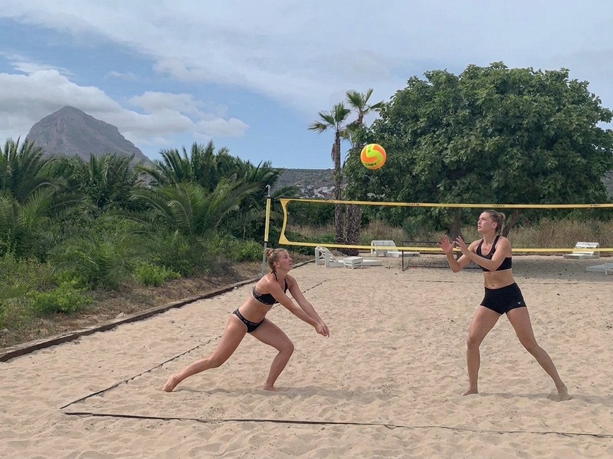 Two players in a beach volleyball rally on the sand court, the Montgó behind them